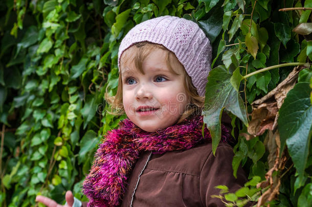 迷人的小女孩，戴着帽子和外套，站在墙上，拿着野生葡萄，阳光明媚的秋日玩耍和享受