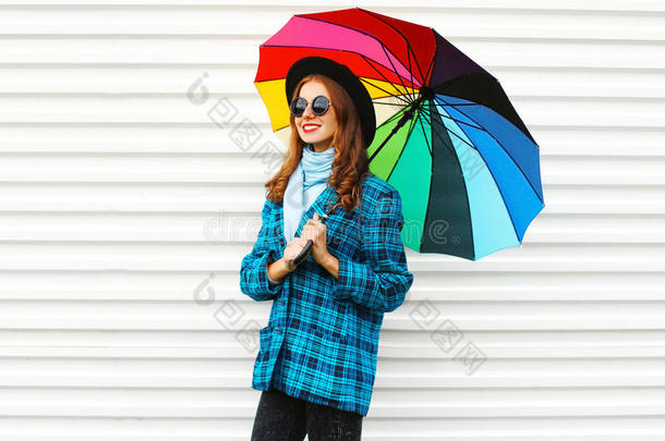 时尚漂亮的微笑女人拿着五颜六色的雨伞，戴着黑色的帽子，格子外套外套，白色的