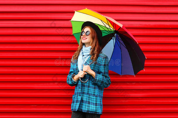 时尚漂亮的年轻微笑的女人拿着五颜六色的雨伞，戴着黑色的帽子，格子<strong>外套外套</strong>，<strong>红色</strong>的