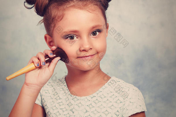 可爱的漂亮的小女孩在脸上涂上色调的化妆品，用化妆刷和快乐的微笑。 色调特写肖像