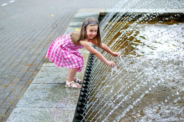 可爱的小女孩在炎热和阳光明媚的夏天玩城市喷泉