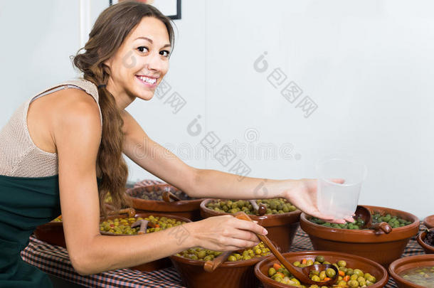 女卖家在食品店用勺子采摘橄榄