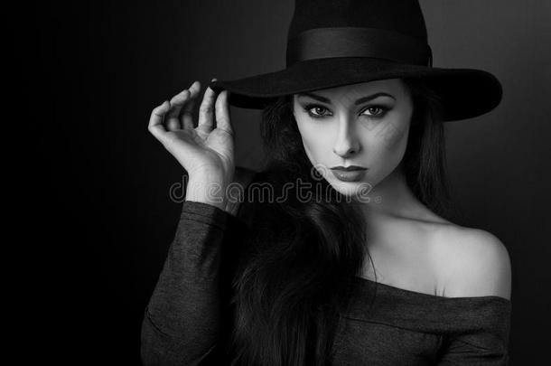 优雅的化妆女子戴着时尚帽子，在黑影背景上摆姿势。 特写肖像。 黑白肖像