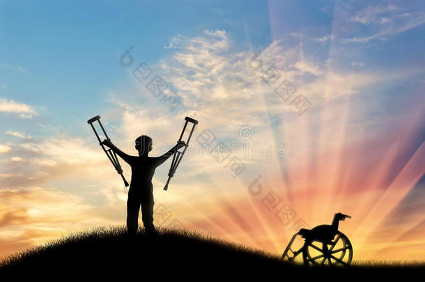 在山上和日落时，在轮椅旁边用拐杖残疾的孩子。