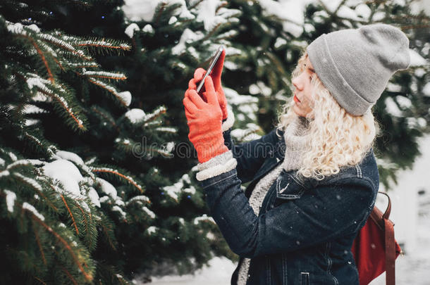 金发卷发女孩在智能手机上拍照，冬天