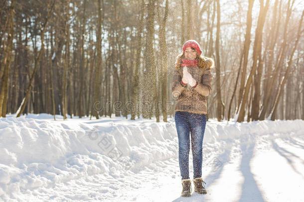 美丽的女孩在寒冷的冬天公园里吹雪。 在户外。 飞舞的雪花。