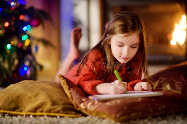 可爱的小女孩在圣诞节的壁炉旁给圣诞老人写了一封信