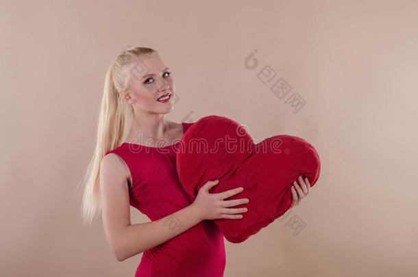 美丽的年轻女人穿着一件鲜红的苗条连衣裙拥抱着一颗毛绒绒的心