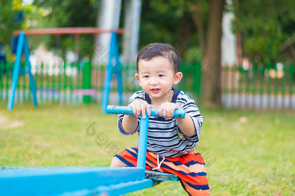 亚洲小孩在阳光下在操场上骑<strong>跷跷板</strong>，