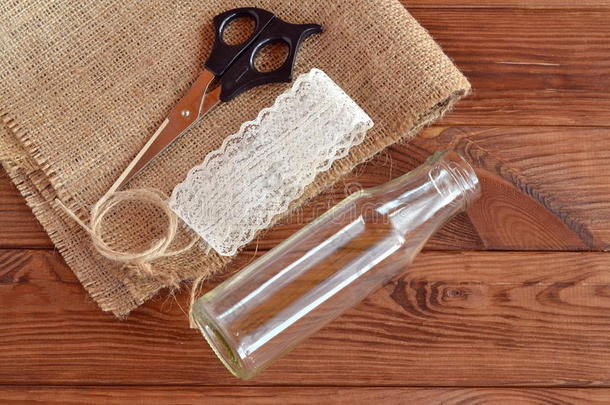 玻璃瓶，剪刀，麻布，绳子，花边。 准备手工花瓶。 乡村风格。 DIY的概念。 棕色木制桌子