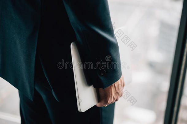 穿着正式西装的人的手拿着笔记本电脑