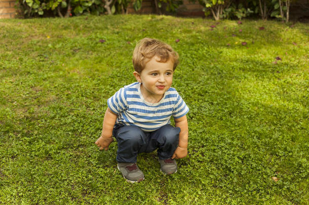 全镜头肖像可爱的笑脸男孩蹲在草地上