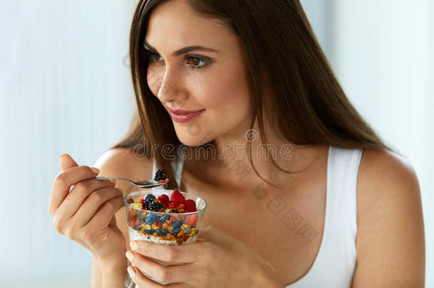 美丽的女人吃酸奶，浆果和谷类食品。 健康的饮食