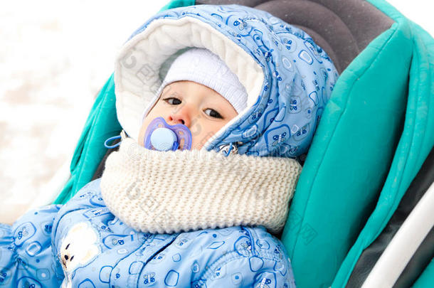 宝贝开心地笑着，在一个下雪的冬天公园里散步，坐在一个温暖的婴儿车里，带着羊皮罩