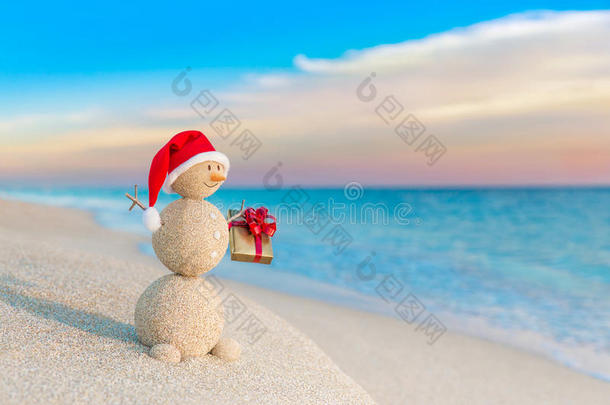 圣诞老人戴着圣诞帽在日落海滩送礼物