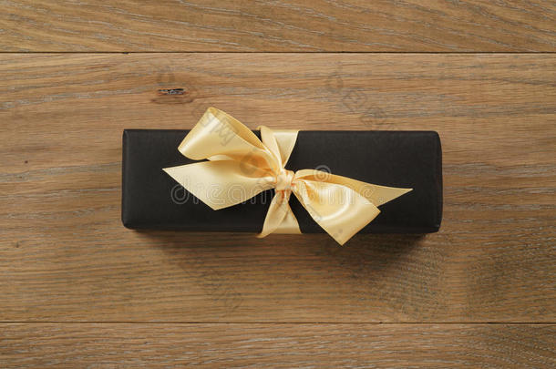 黑色矩形礼品盒，<strong>香槟色</strong>丝带蝴蝶结在木制橡木桌子上，从上面