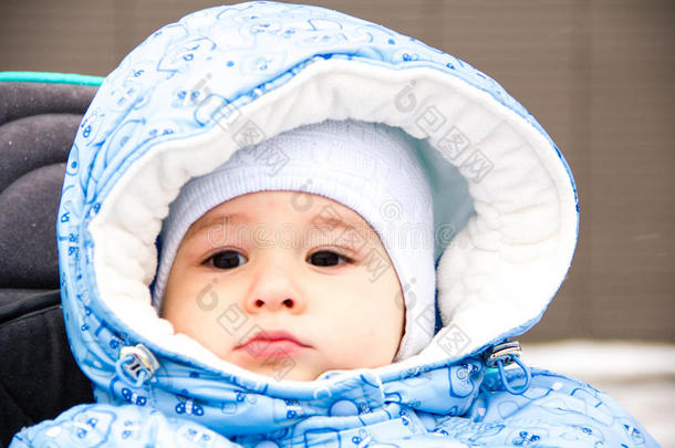 宝贝开心地笑着，在一个下雪的冬天公园里散步，坐在一个温暖的婴儿车里，带着羊皮罩