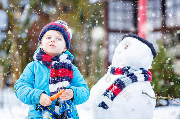 有趣的男孩穿着五颜六色的衣服在户外堆雪人