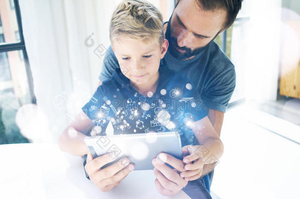 父亲和他的小儿子在移动电脑上一起玩，在室内休息。胡须男和小男孩使用平板电脑