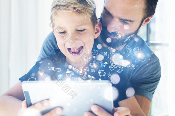 特写照片，小男孩和父亲坐在桌子上，在现代家庭中使用PC平板电脑。童年梦想图标