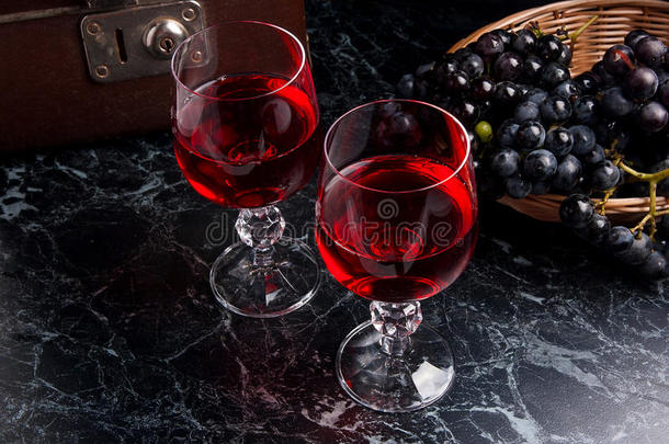 深色大理石背景上的一杯红酒。 背景上的一簇蓝色葡萄。。