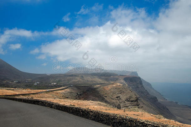 海上悬崖上的沥青路通过火山山山坡<strong>消失</strong>在地平线上。 蓝色上的白云