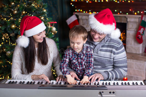 家庭-母亲，父亲和孩子戴着圣诞老人的帽子圣诞节背景下弹钢琴