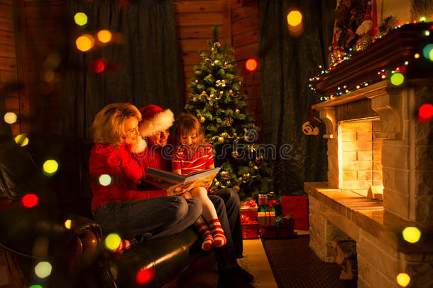 家庭阅<strong>读故事</strong>，坐在沙发前的壁炉在圣诞节装饰的房子内部