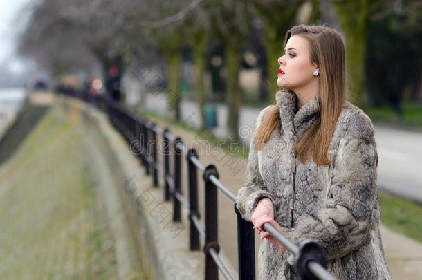 穿着毛皮大衣的优雅女孩独自在冬天的城市小巷里散步