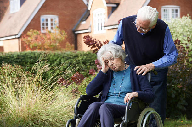 坐轮椅的沮丧的老年妇女被丈夫推着