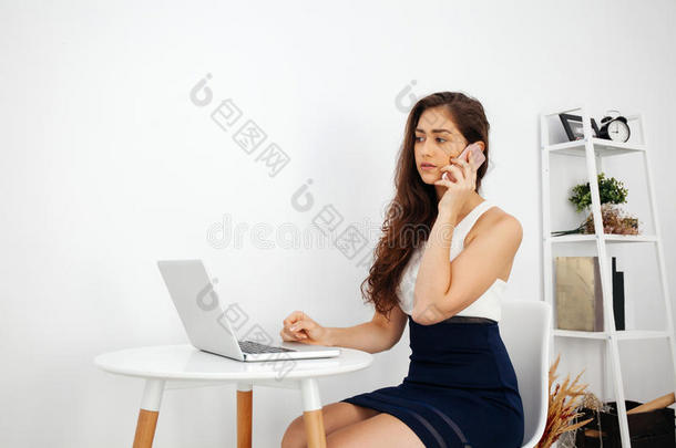 美丽的白种人女人在电话中交谈，同时在白色桌子上使用笔记本电脑，在<strong>干净</strong>的家庭办公室和复印<strong>空间</strong>