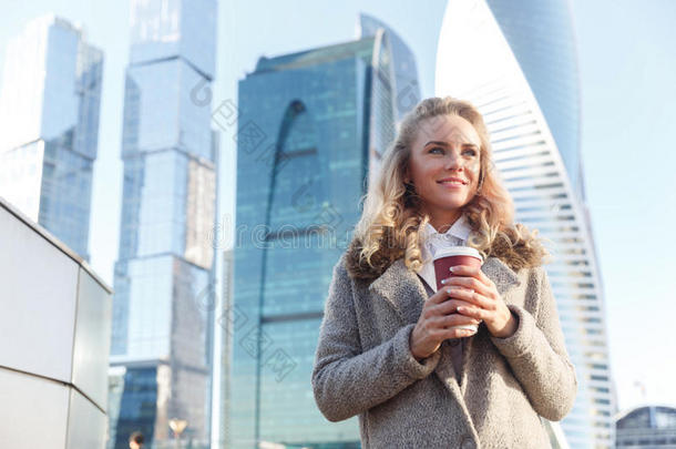 美丽的年轻女人拿着咖啡在摩天大楼的背景上