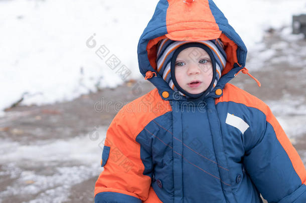 迷人的小男孩玩第一场雪。 他微笑着看着雪人。 厚厚的蓝色橙色连体裤，明亮的条纹