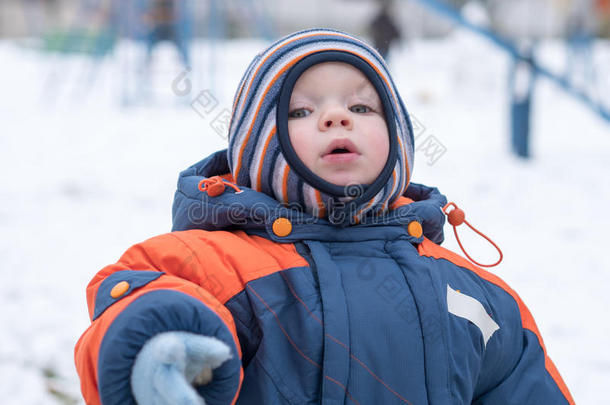 迷人的小男孩玩第一场雪。 他微笑着看着雪人。 厚厚的蓝色橙色<strong>连体</strong>裤，明亮的条纹