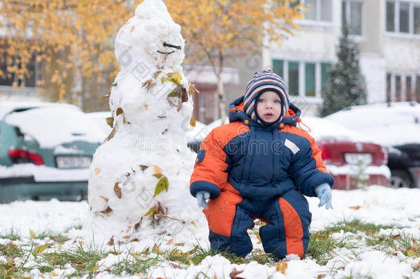 迷人的小男孩玩第一场雪。 他微笑着看着雪人。 厚厚的蓝色橙色<strong>连体</strong>裤，明亮的条纹