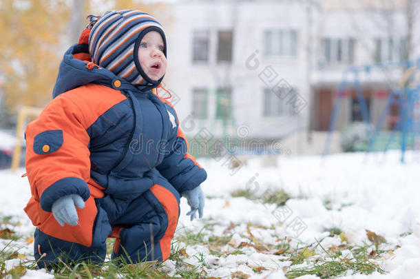 迷人的小男孩<strong>玩</strong>第一场<strong>雪</strong>。 他微笑着看着<strong><strong>雪</strong>人</strong>。 厚厚的蓝色橙色连体裤，明亮的条纹