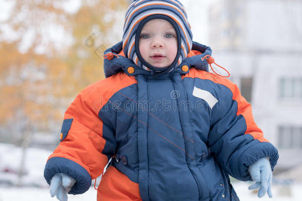 迷人的小男孩<strong>玩</strong>第一场<strong>雪</strong>。 他微笑着看着<strong><strong>雪</strong>人</strong>。 厚厚的蓝色橙色连体裤，明亮的条纹