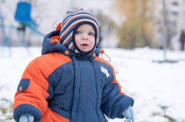 迷人的小男孩<strong>玩</strong>第一场<strong>雪</strong>。 他微笑着看着<strong><strong>雪</strong>人</strong>。 厚厚的蓝色橙色连体裤，明亮的条纹