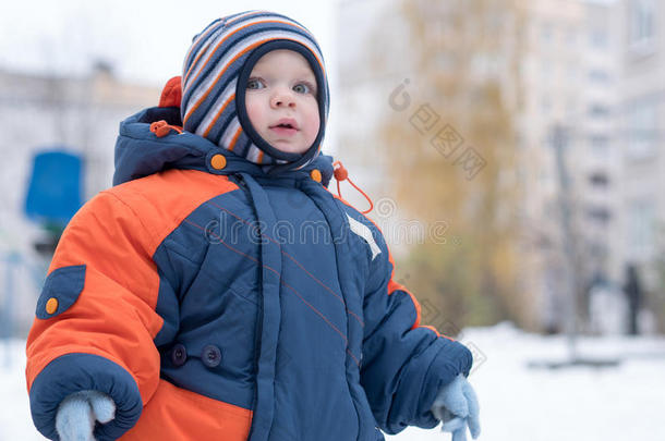 迷人的小男孩玩第一场雪。 他微笑着看着雪人。 厚厚的蓝色橙色连体裤，明亮的条纹