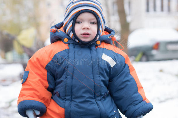 迷人的小男孩玩第一场雪。 他微笑着看着雪人。 厚厚的蓝色橙色连体裤，明亮的条纹