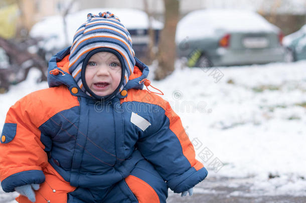 迷人的小男孩玩第一场雪。 他微笑着看着雪人。 厚厚的蓝色橙色连体裤，明亮的条纹