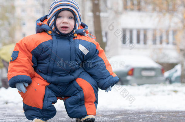 迷人的小男孩<strong>玩</strong>第一场<strong>雪</strong>。 他微笑着看着<strong><strong>雪</strong>人</strong>。 厚厚的蓝色橙色连体裤，明亮的条纹