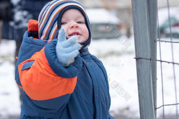迷人的小男孩<strong>玩</strong>第一场<strong>雪</strong>。 他微笑着看着<strong><strong>雪</strong>人</strong>。 厚厚的蓝色橙色连体裤，明亮的条纹