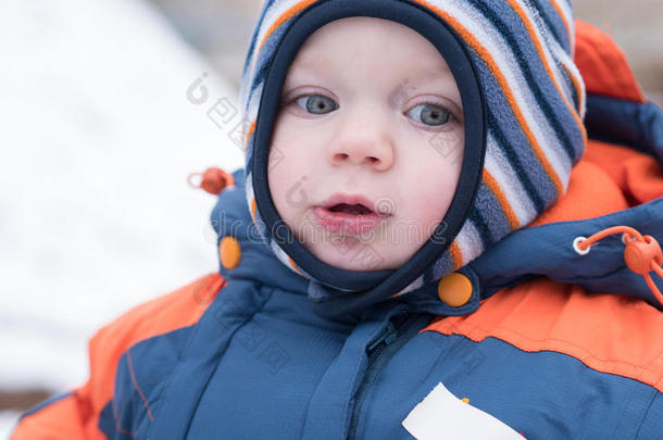 迷人的小男孩玩第一场雪。 他微笑着看着雪人。 厚厚的蓝色橙色<strong>连体</strong>裤，明亮的条纹