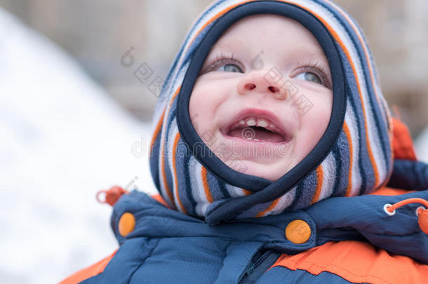 迷人的小男孩玩第一场雪。 他微笑着看着雪人。 厚厚的蓝色橙色连体裤，明亮的条纹
