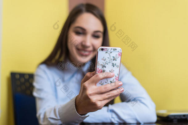 可爱的年轻女人和朋友聊天或用智能手机在线购物。 漂亮的电话盖上粉红色的花。