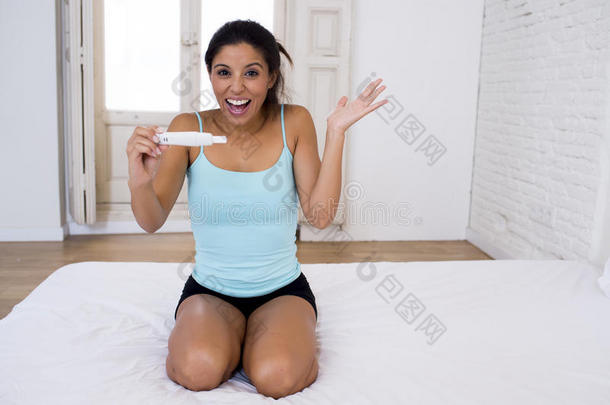 美丽的拉丁女人拿着怀孕测试，看着发现积极的结果，微笑着快乐和兴奋