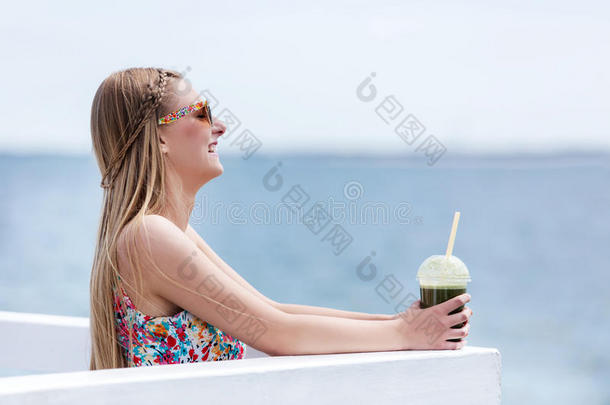 美丽的年轻女人戴着太阳镜喝<strong>绿色蔬菜</strong>冰沙。