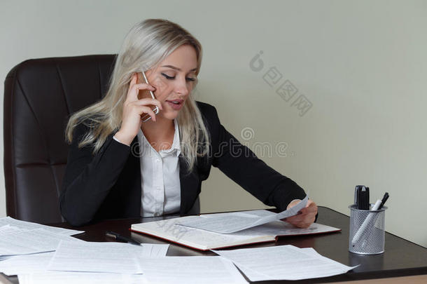 美丽微笑的商务女士在办公桌上工作，拿着文件和打电话。