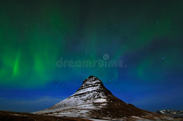 来自冰岛的北极光。 美丽的绿色北极光在深蓝色的夜空与雪峰，柯克朱菲尔